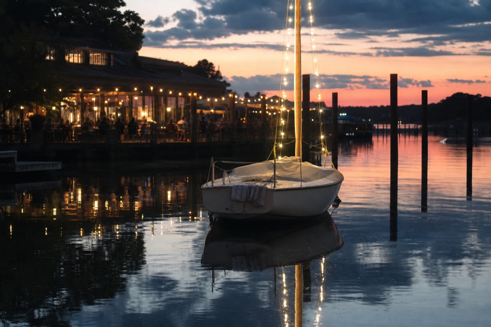A small boat anchored near a waterfront restaurant at dusk, no text, no logos, no people