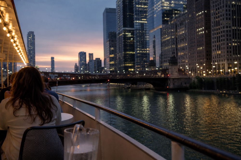 A riverboat moving down a lit city waterway at dusk, no text, no logos, no people