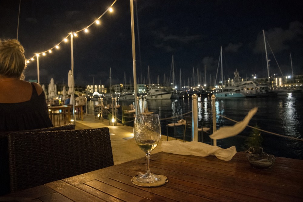 A waterfront bar terrace at night with string lights along a marina, no text, no logos, no people